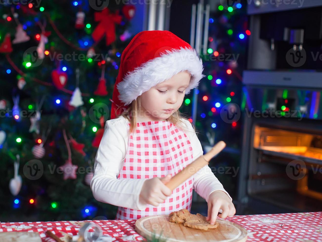 Adorable little girl in Santa hat baking gingerbread Christmas cookies at home photo