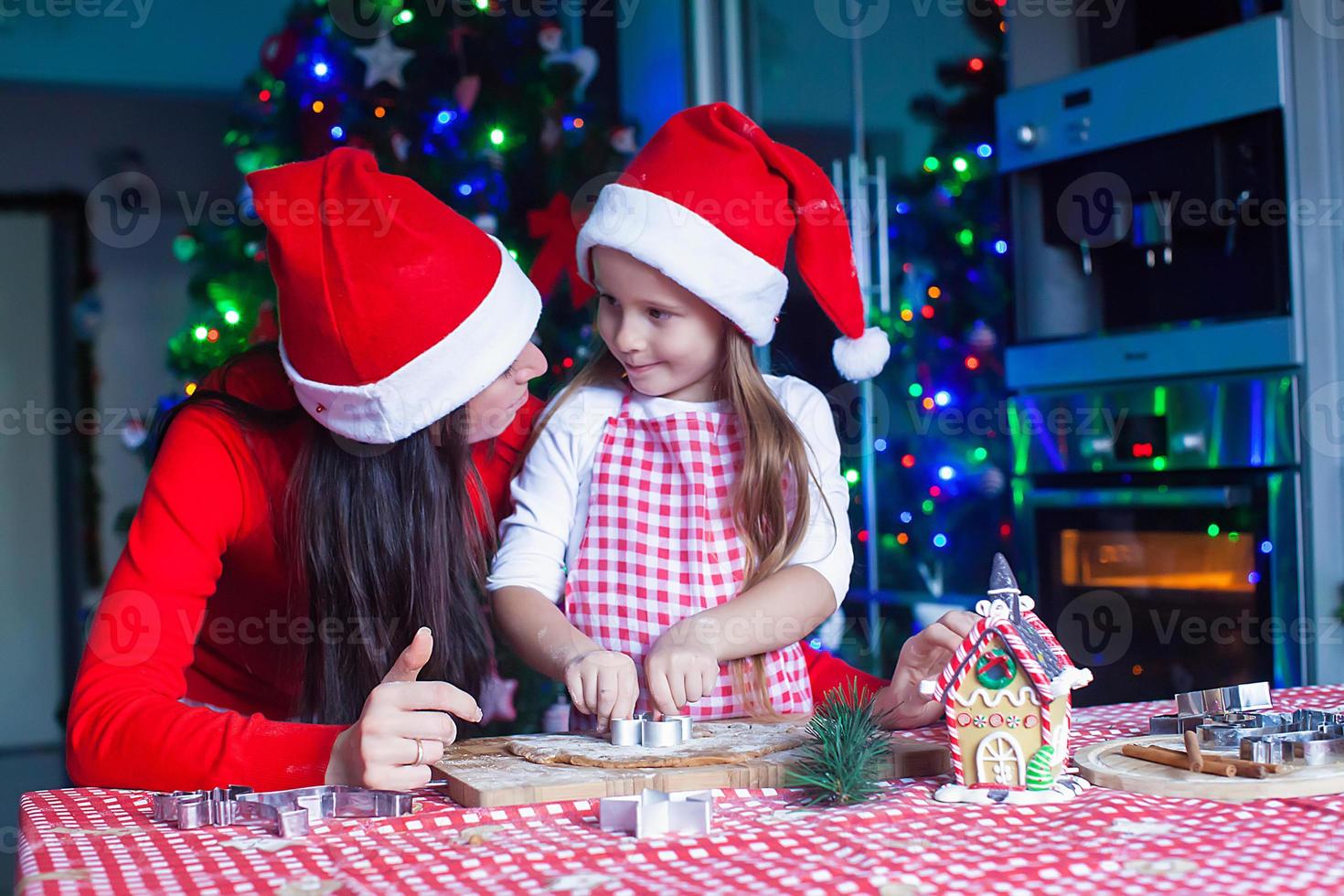 Adorable girl with her mother baking Christmas cookies in the kitchen photo