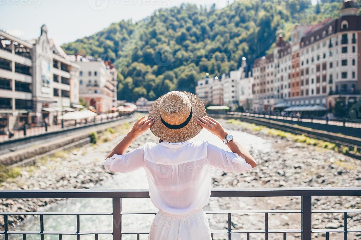 chica feliz con sombrero en el terraplén de un río de montaña en una ciudad europea. foto