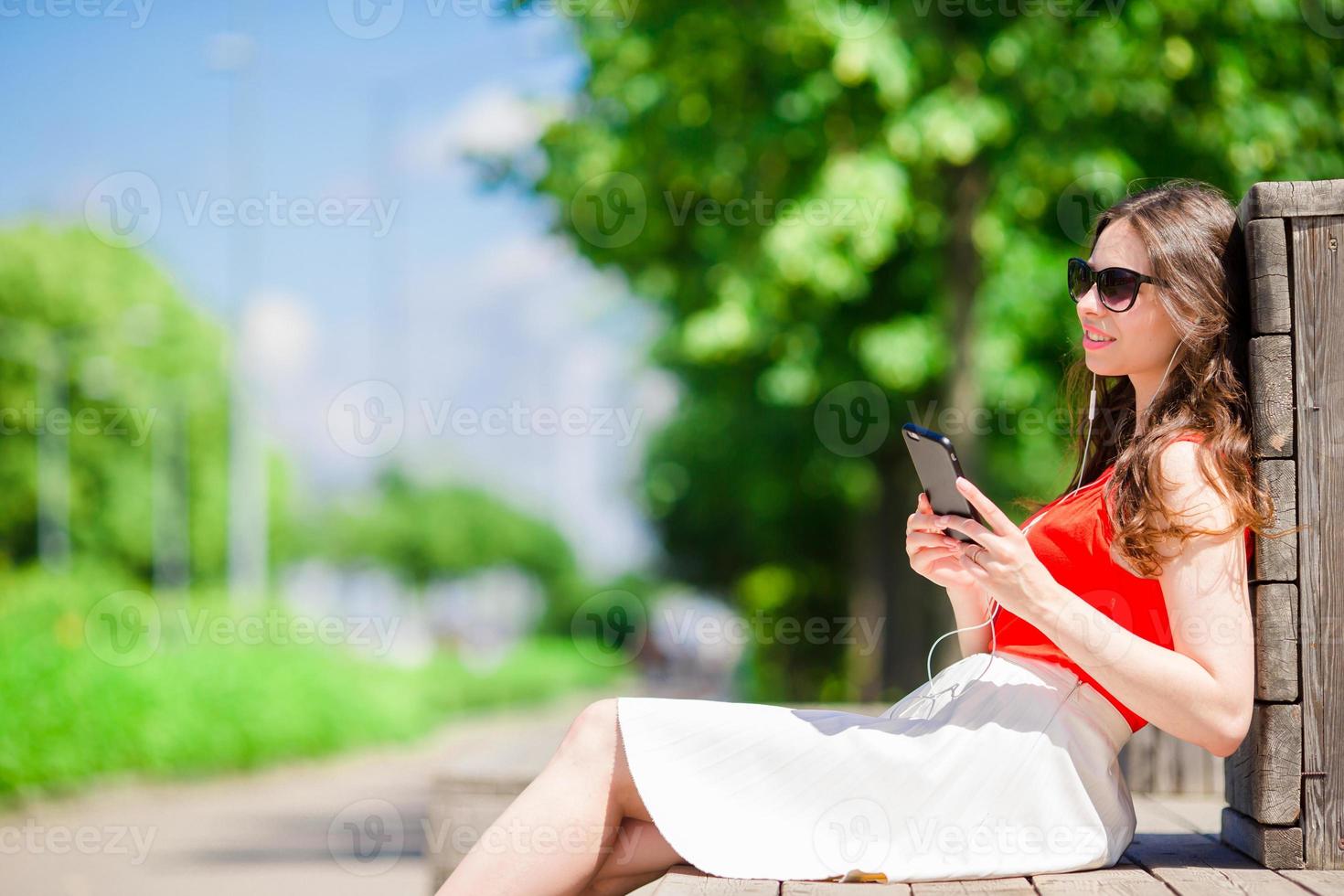 hermosa chica escuchando música por teléfono inteligente en vacaciones de verano. joven turista atractivo con teléfono móvil al aire libre disfrutando de las vacaciones. foto