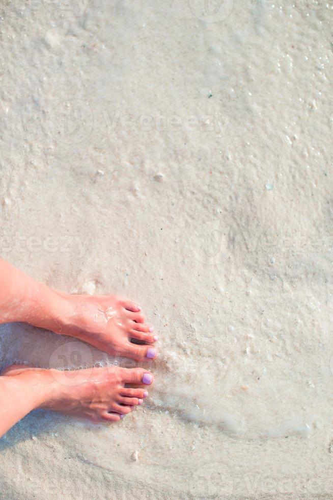 pies de mujer en la playa de arena blanca en aguas poco profundas foto