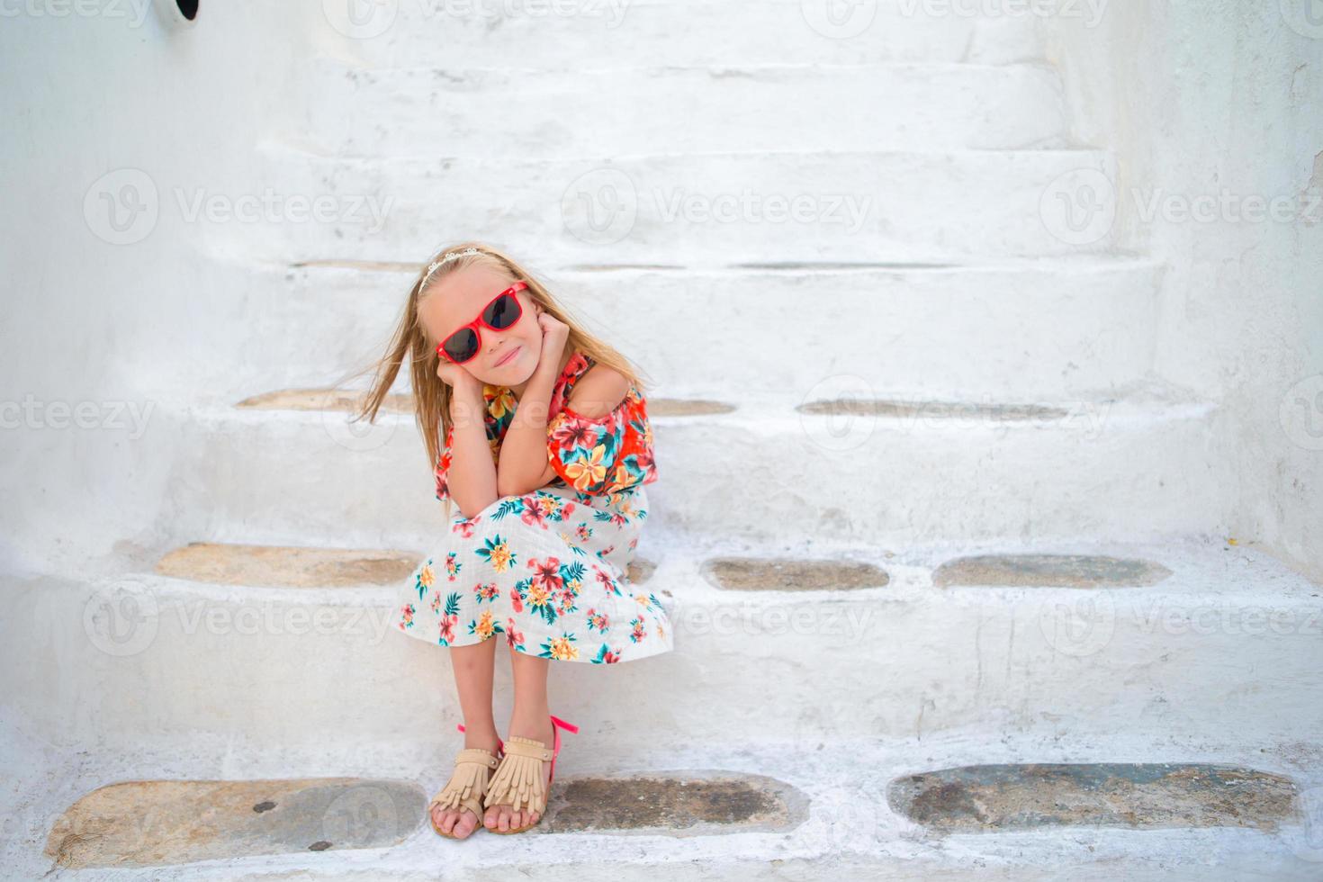 Little cute girl portrait outdoors in old greek village. Kid at street of typical greek traditional village with white walls and colorful doors on Mykonos Island, in Greece photo