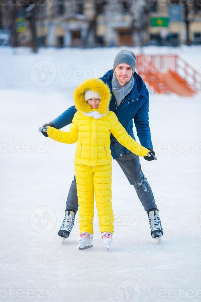 Little adorable girl with father learning to skate on ice-rink photo