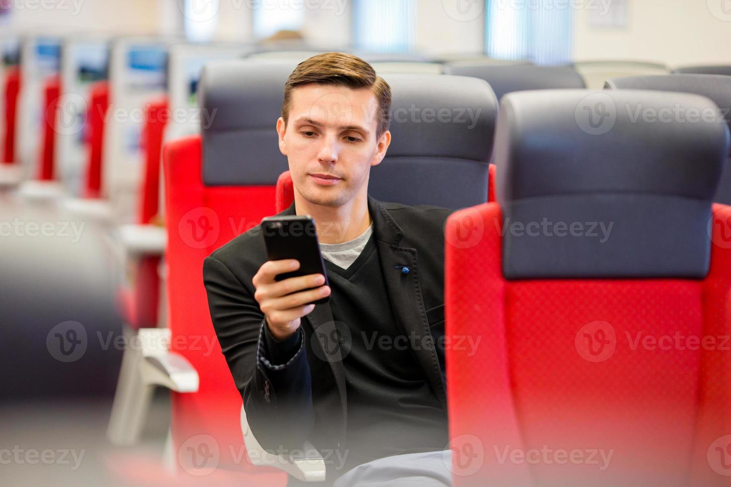 Young tourist man traveling by train. Passenger writing a message on cellphone while traveling by express train photo