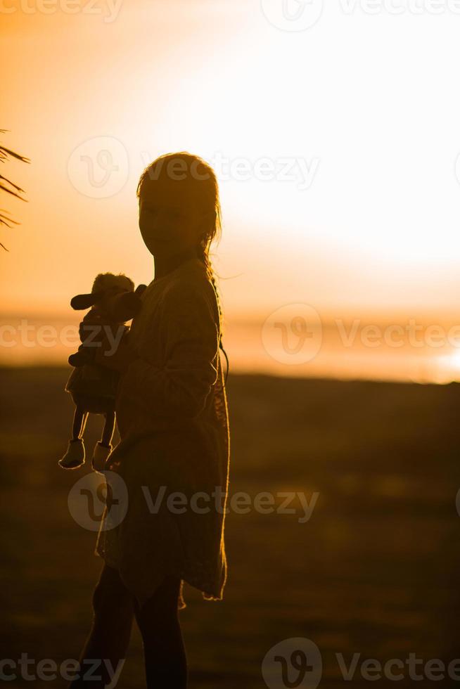 adorable niña feliz caminando en la playa blanca al atardecer. foto