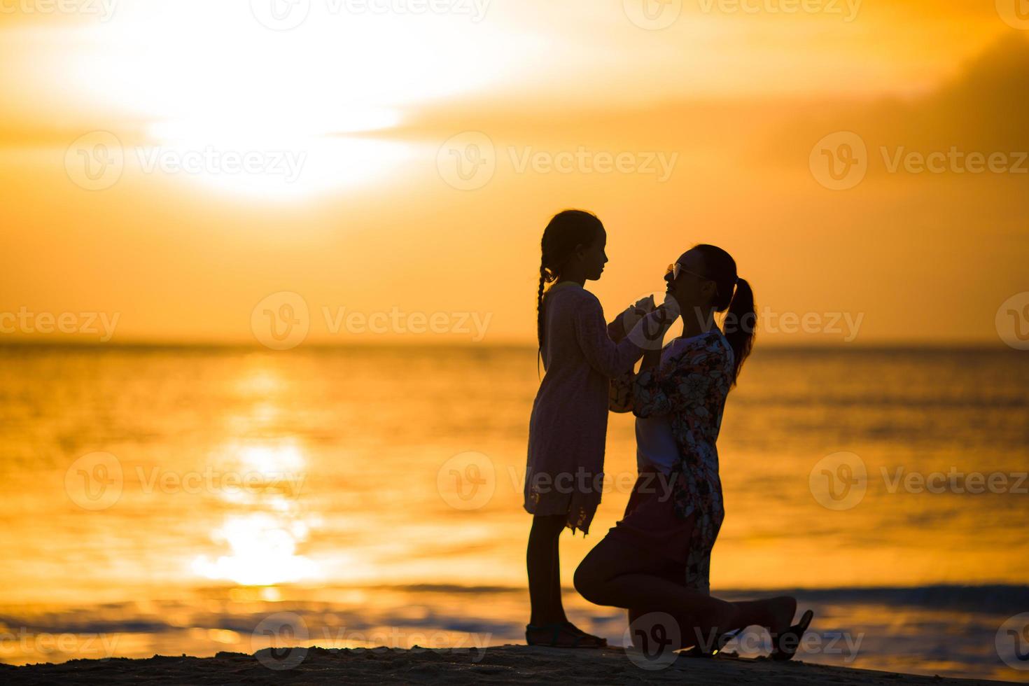 Little girl and happy mother silhouette in the sunset at the beach photo
