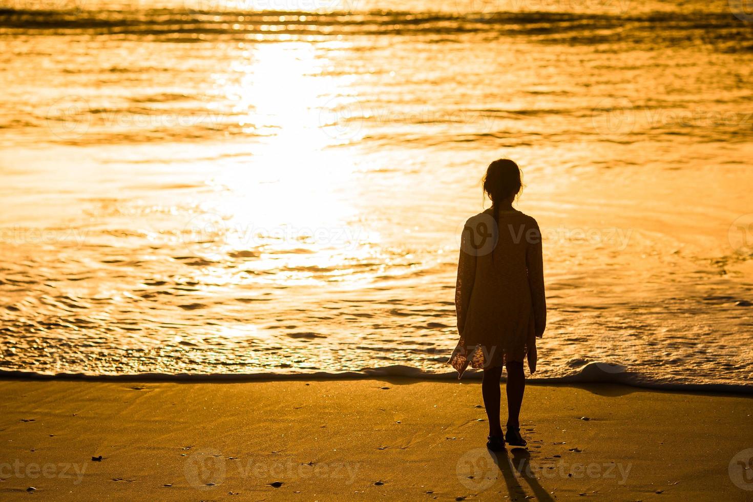 Adorable happy little girl walking on white beach at sunset. photo