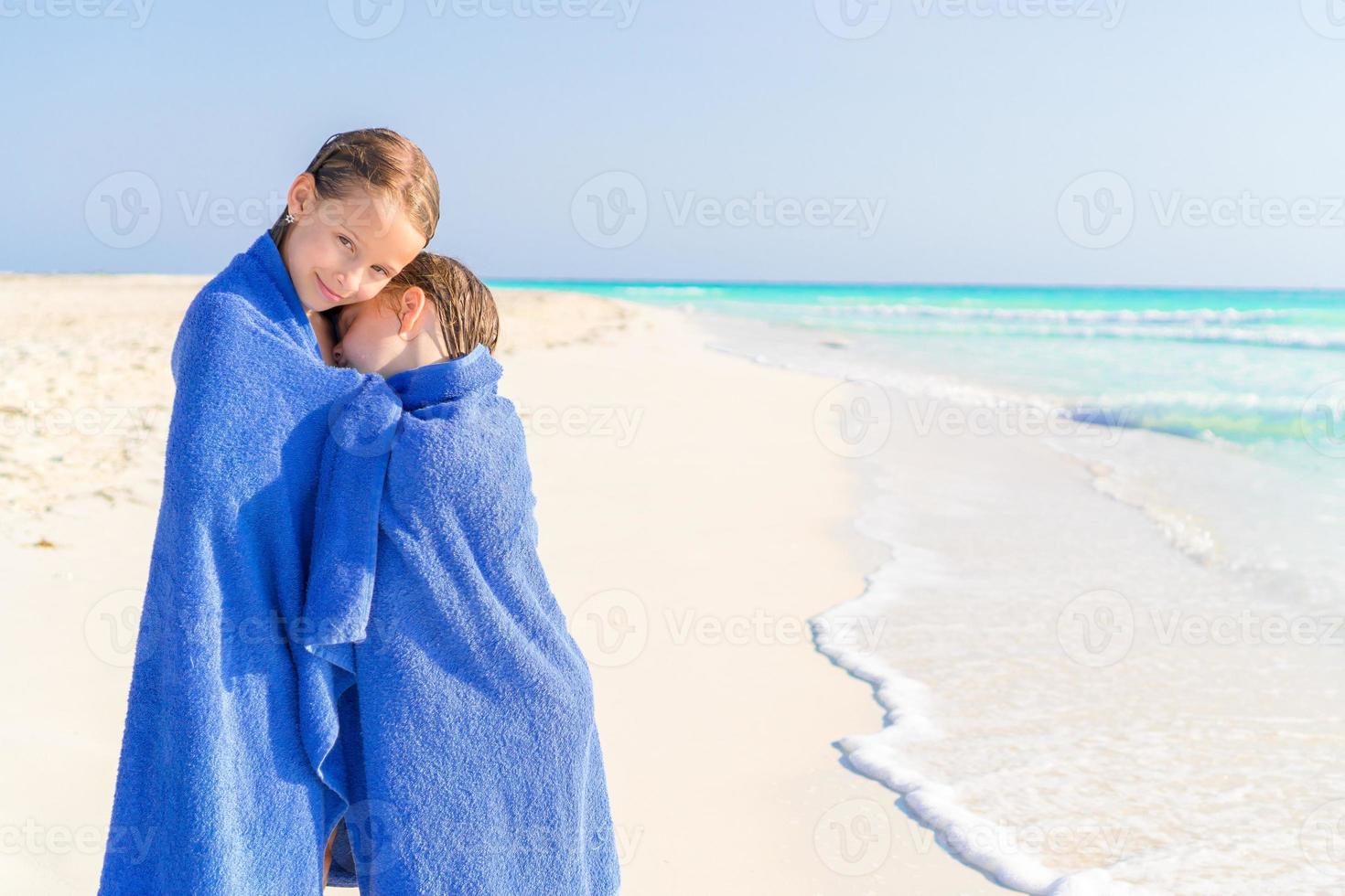 Adorable little girls wrapped in towel at tropical beach after swimming in the sea photo