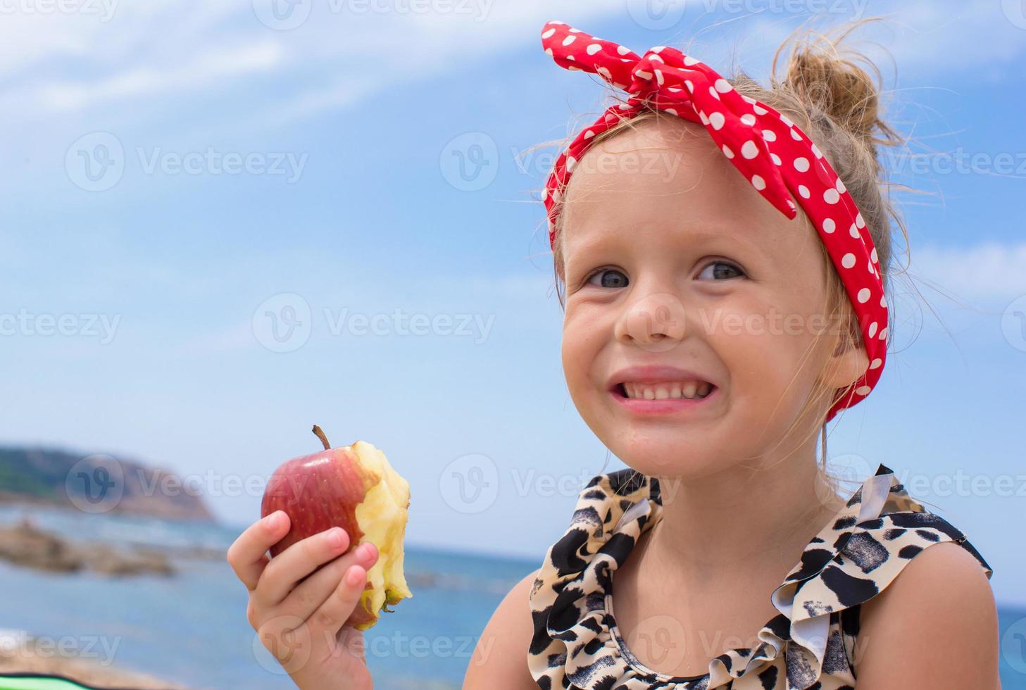 Adorable little girl have fun eating an apple photo