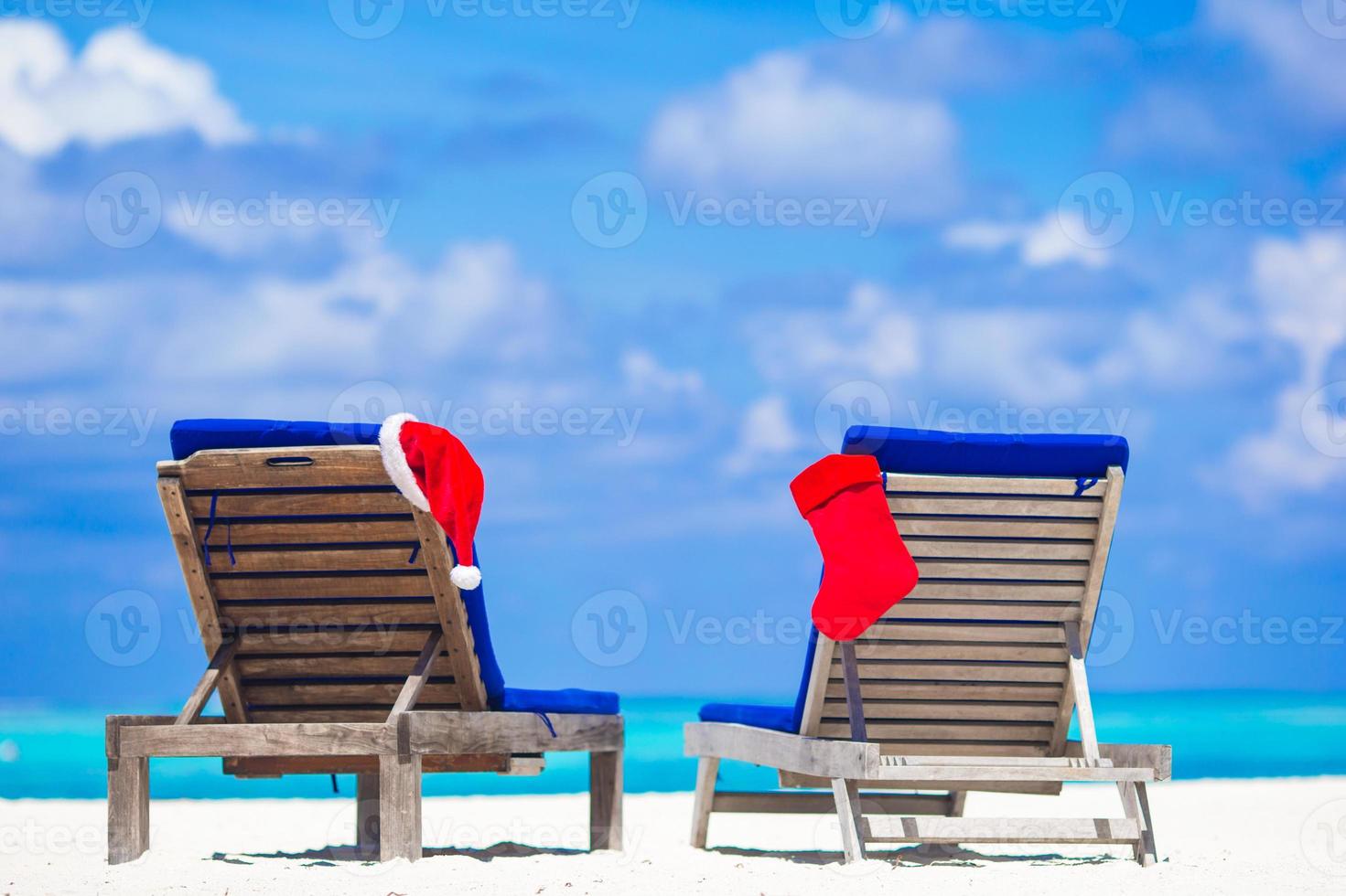 Red Christmas stocking and Santa Hat on sunloungers at tropical white beach photo