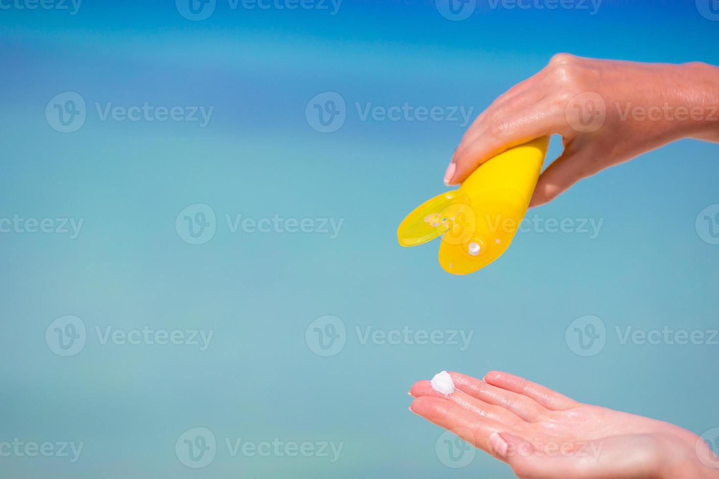 Female hands with suncream bottle background blue sea photo