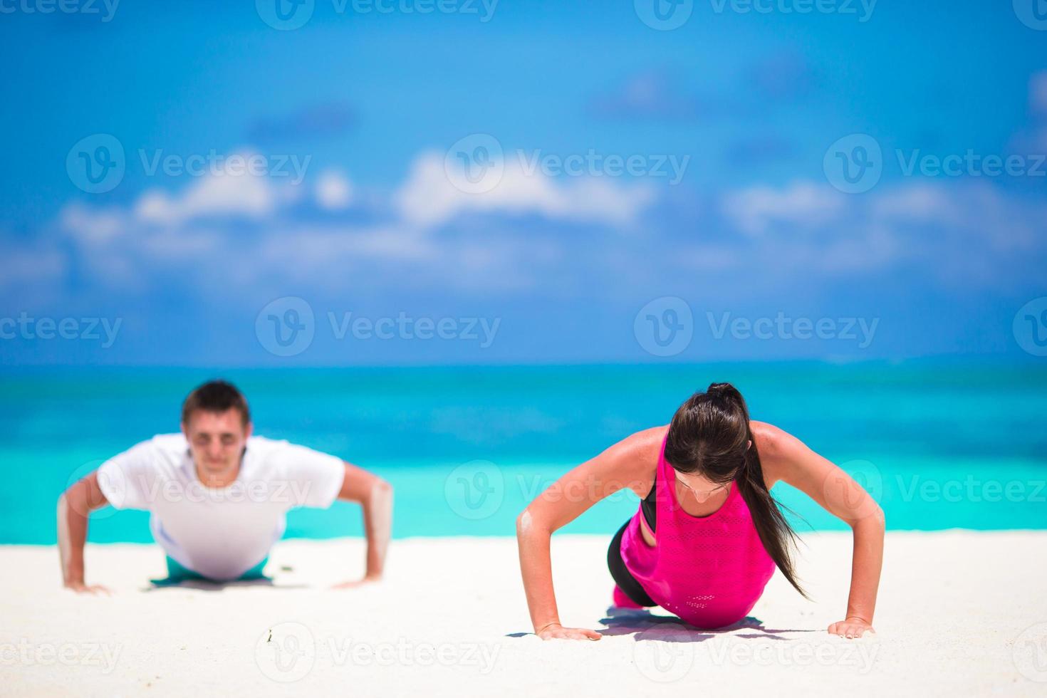 Young fitness couple doing push-ups during outdoor cross training workout on tropical beach photo