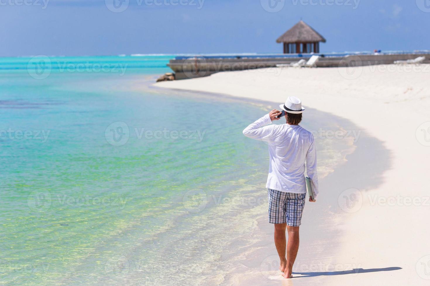 joven hombre de negocios llamando por teléfono celular en playa blanca foto