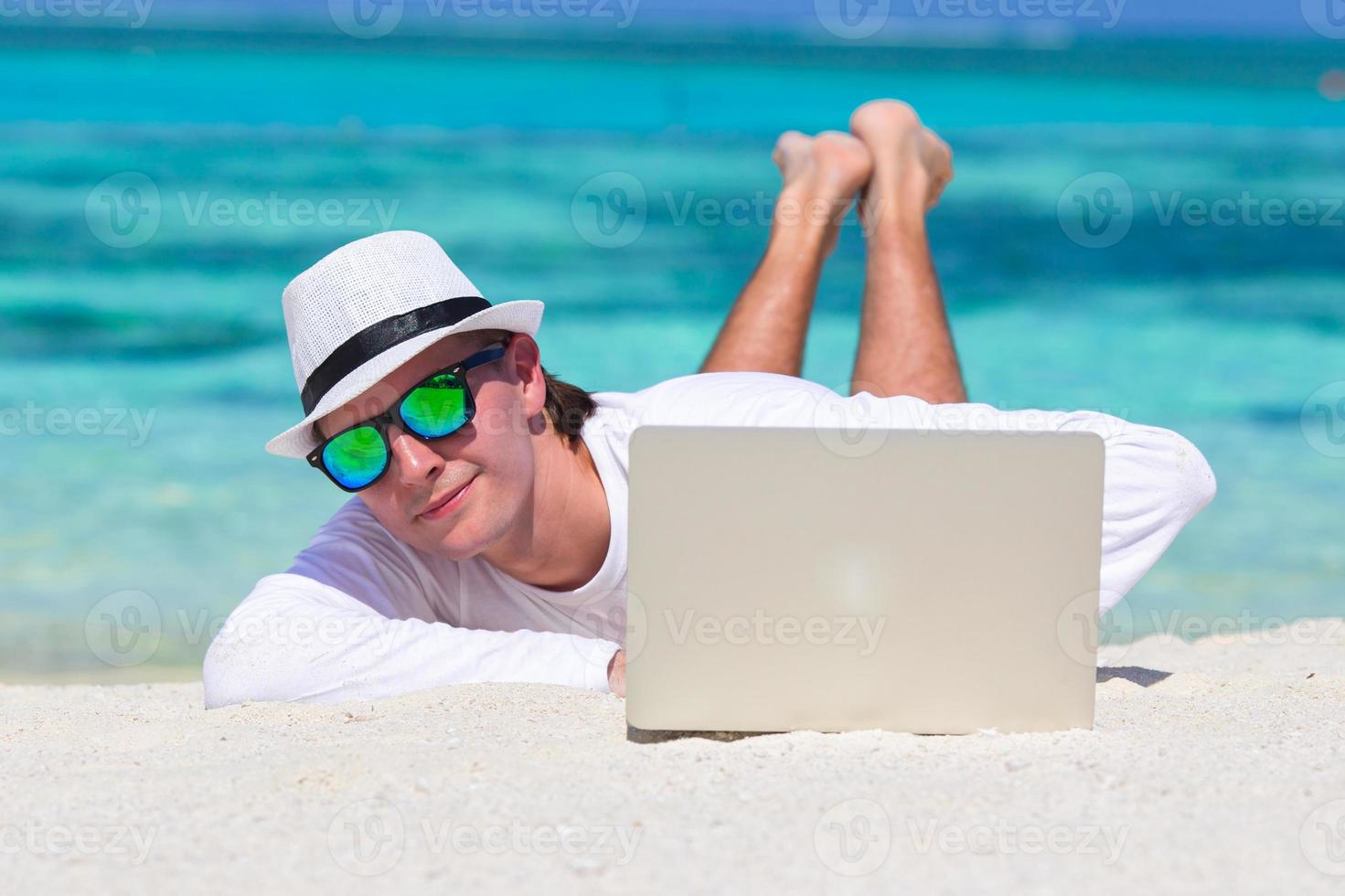 Young man working on laptop at tropical beach near water villa photo
