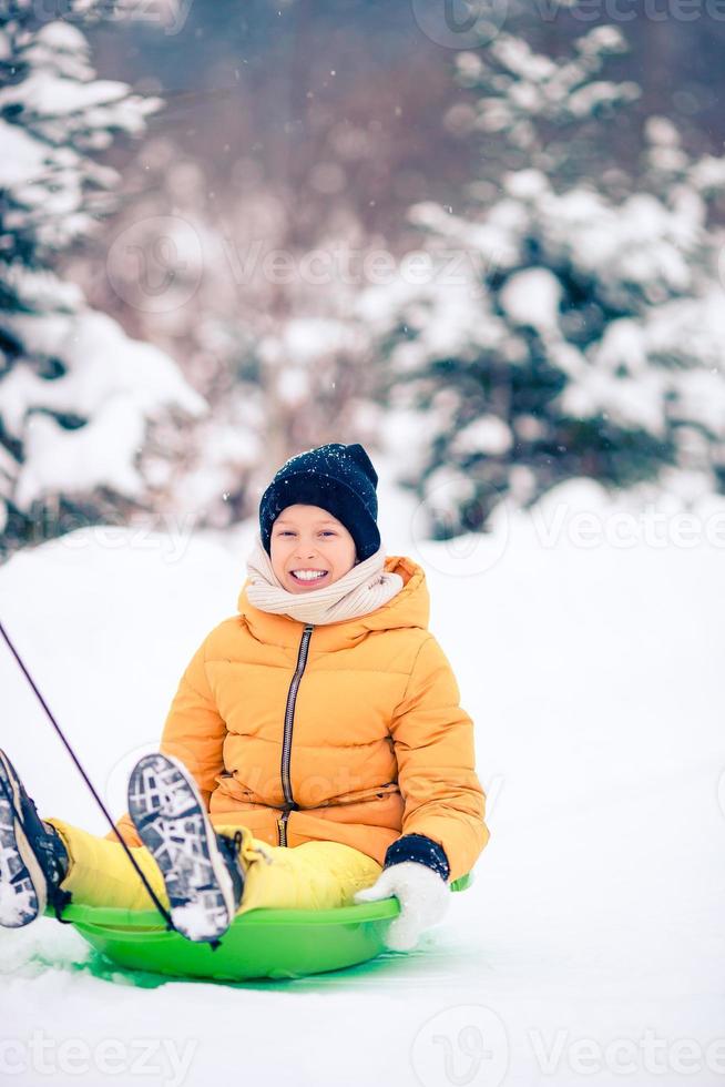 Adorable little happy girl sledding in winter snowy day. photo