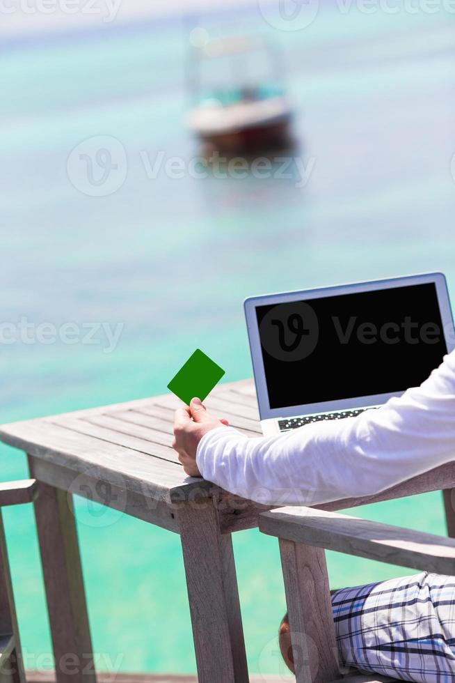 Close-up of green credit card and computer on table background the sea photo