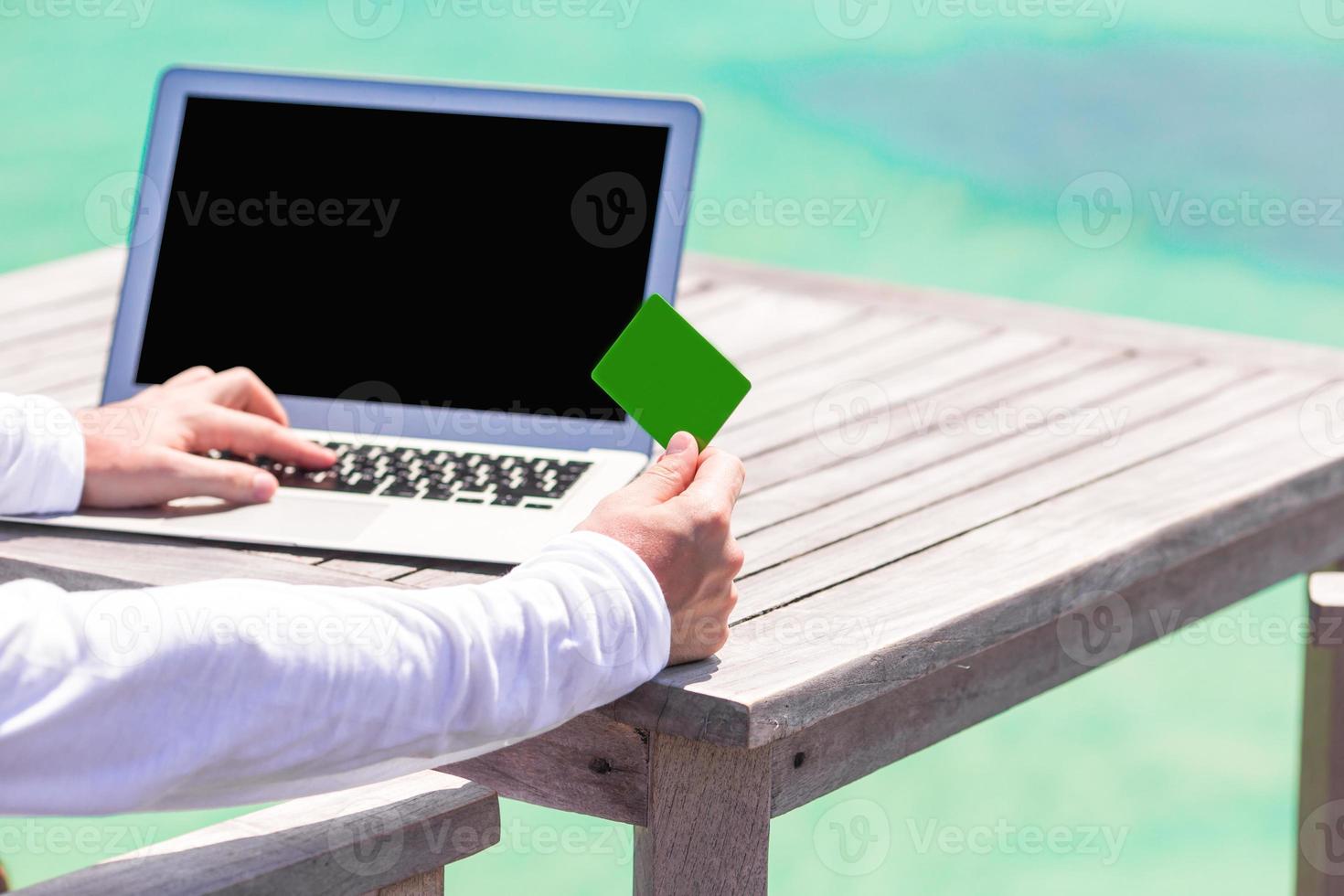 Closeup of green credit card and computer on table background the sea photo