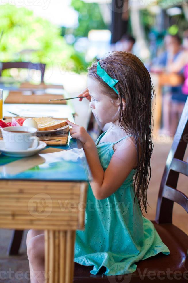 Adorable little girl having breakfast at outdoor cafe photo