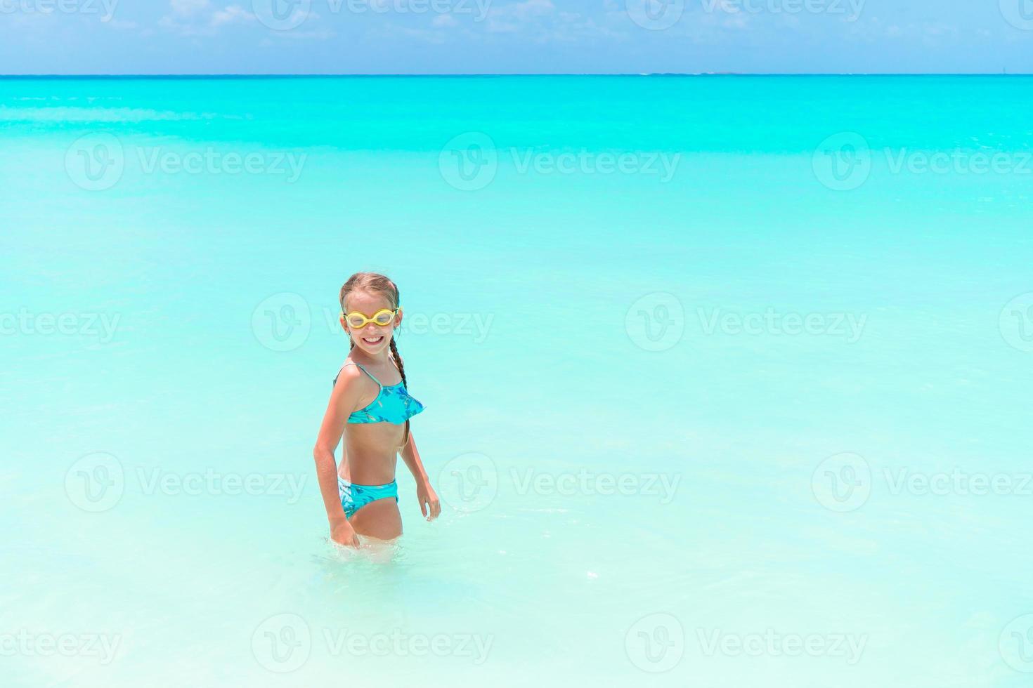 Little happy girl splashing and having fun in the shallow water. Kid in swimsuit playing with sand photo