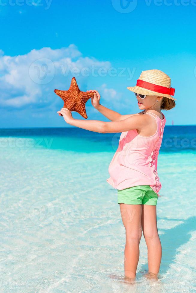 Adorable little girl with starfish on white empty beach photo