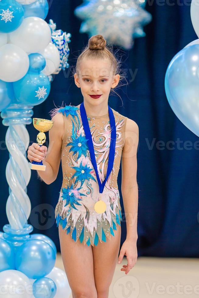 pequeña gimnasta con sus premios deportivos en la alfombra de gimnasia rítmica foto