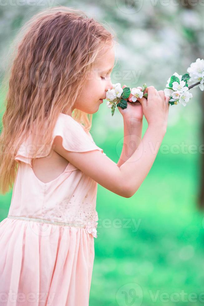 adorable niñita disfrutando del olor en un florido jardín de primavera de cerezos foto