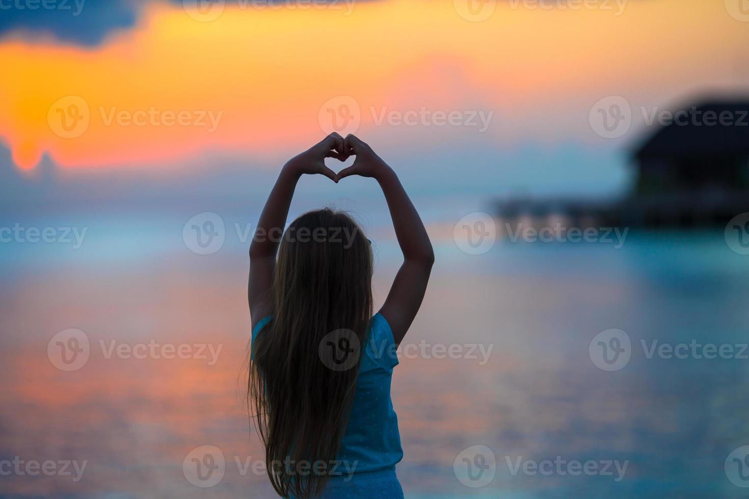Silhouette of heart made by kids hand at sunset photo