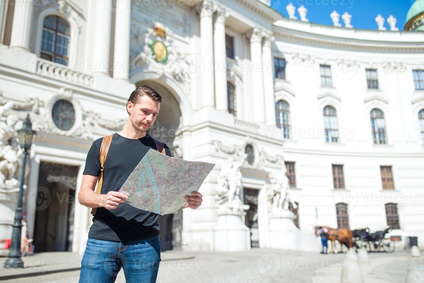 Man tourist with a city map and backpack in Europe street. Caucasian boy looking with map of European city. photo