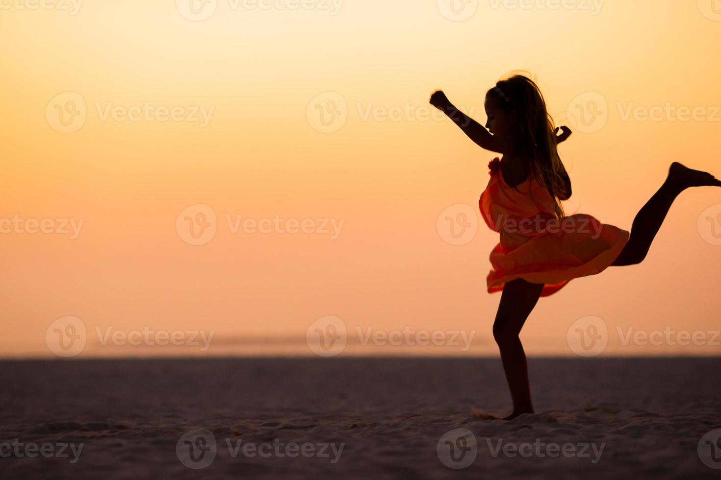 Silhouette of sporty little girl on white beach at sunset photo