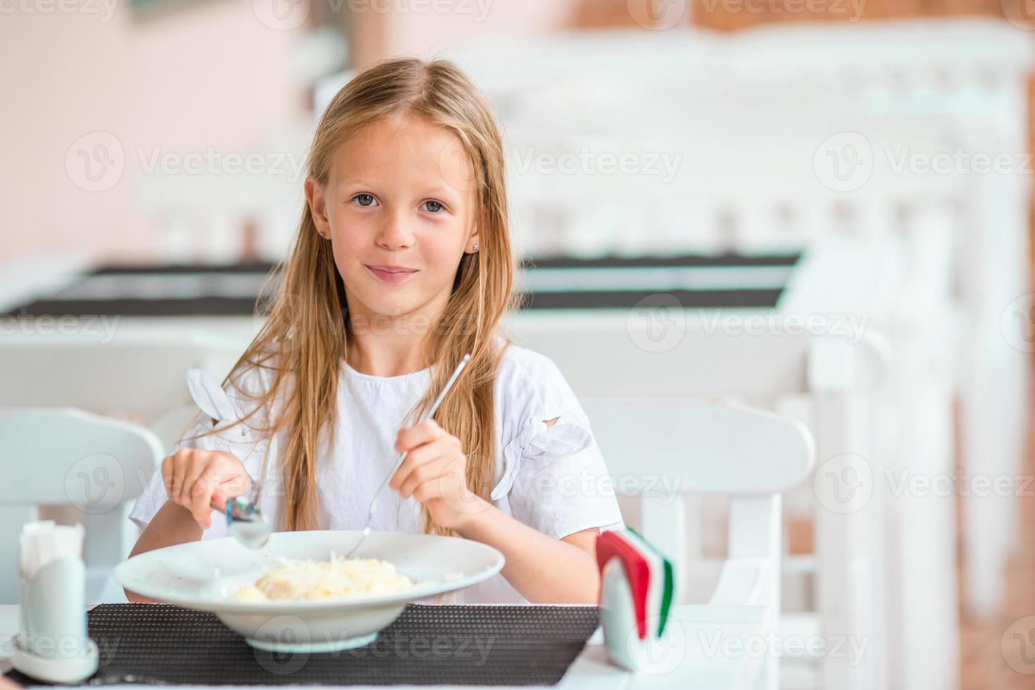 Adorable little girl having dinner at outdoor cafe photo