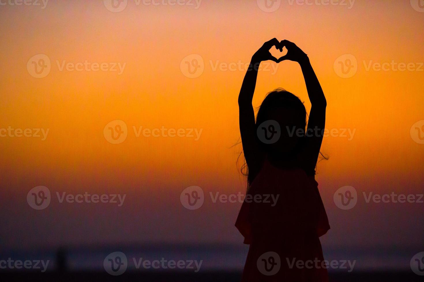 Silhouette of little girl making heart at sunset on the beach photo