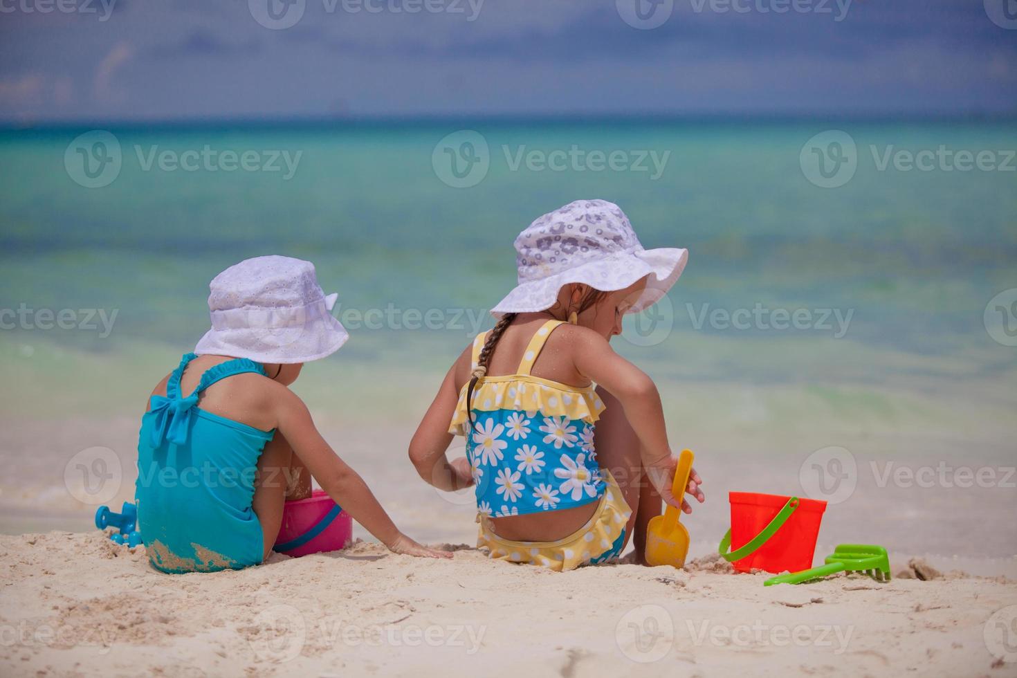 Back view of Two little sisters in nice swimsuits playing on sandy beach photo