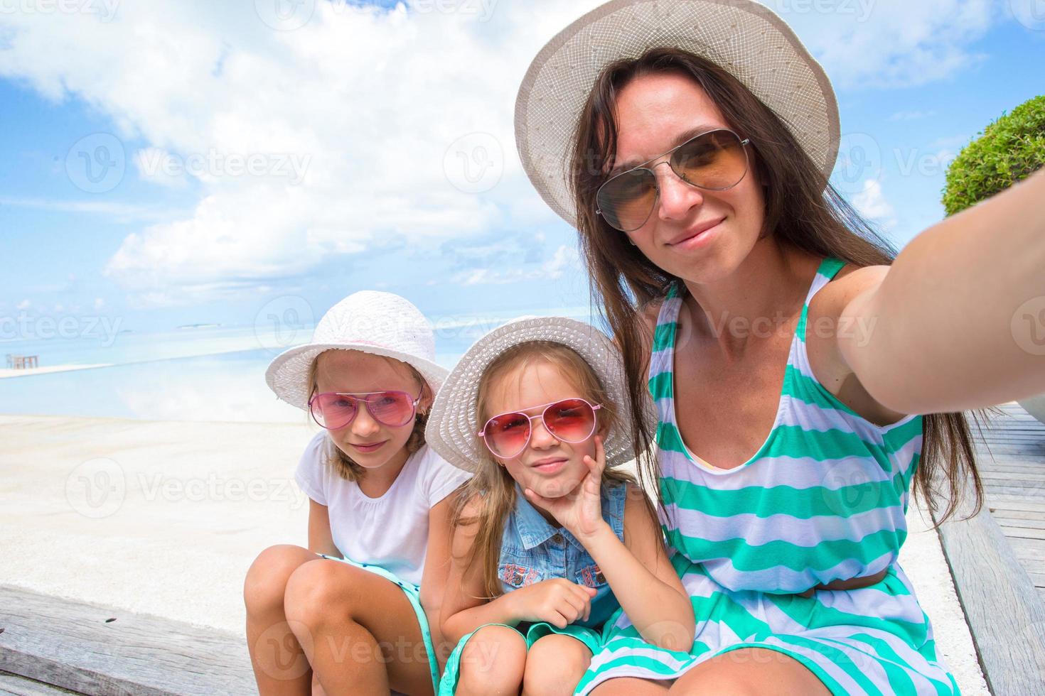 madre y niñas tomando selfie en playa tropical foto