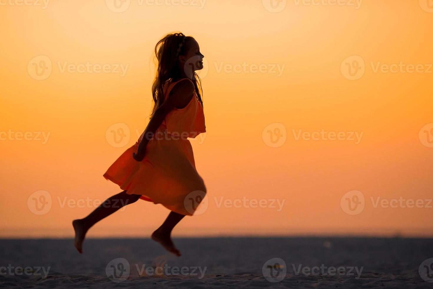 Silhouette of adorable little girl on white beach at sunset photo