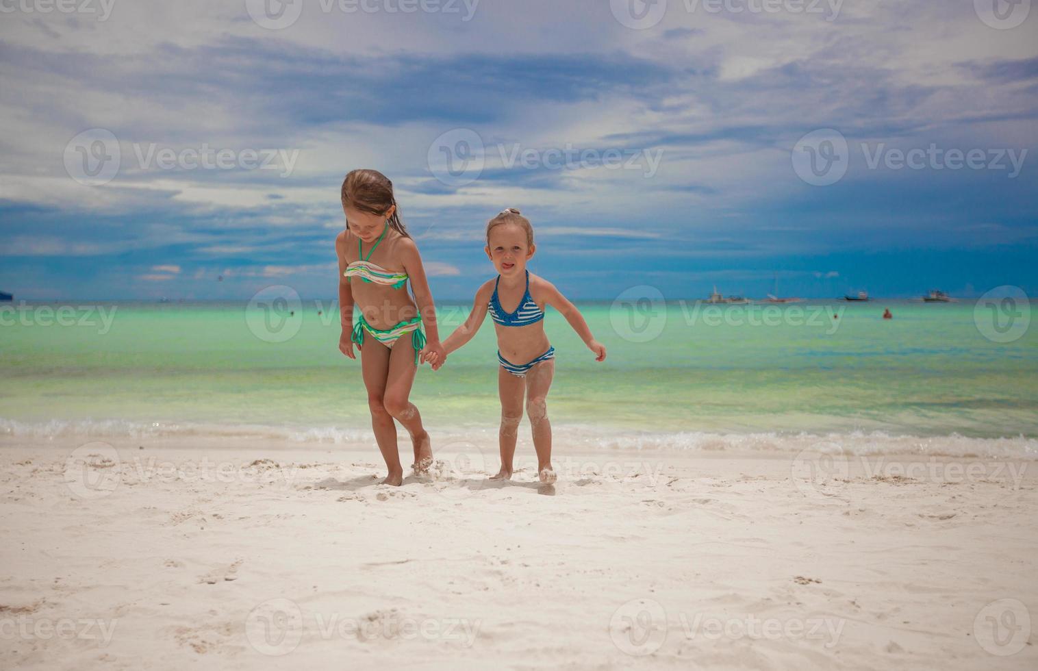 Two little sisters in nice swimsuits out of the sea at tropical exotic beach photo