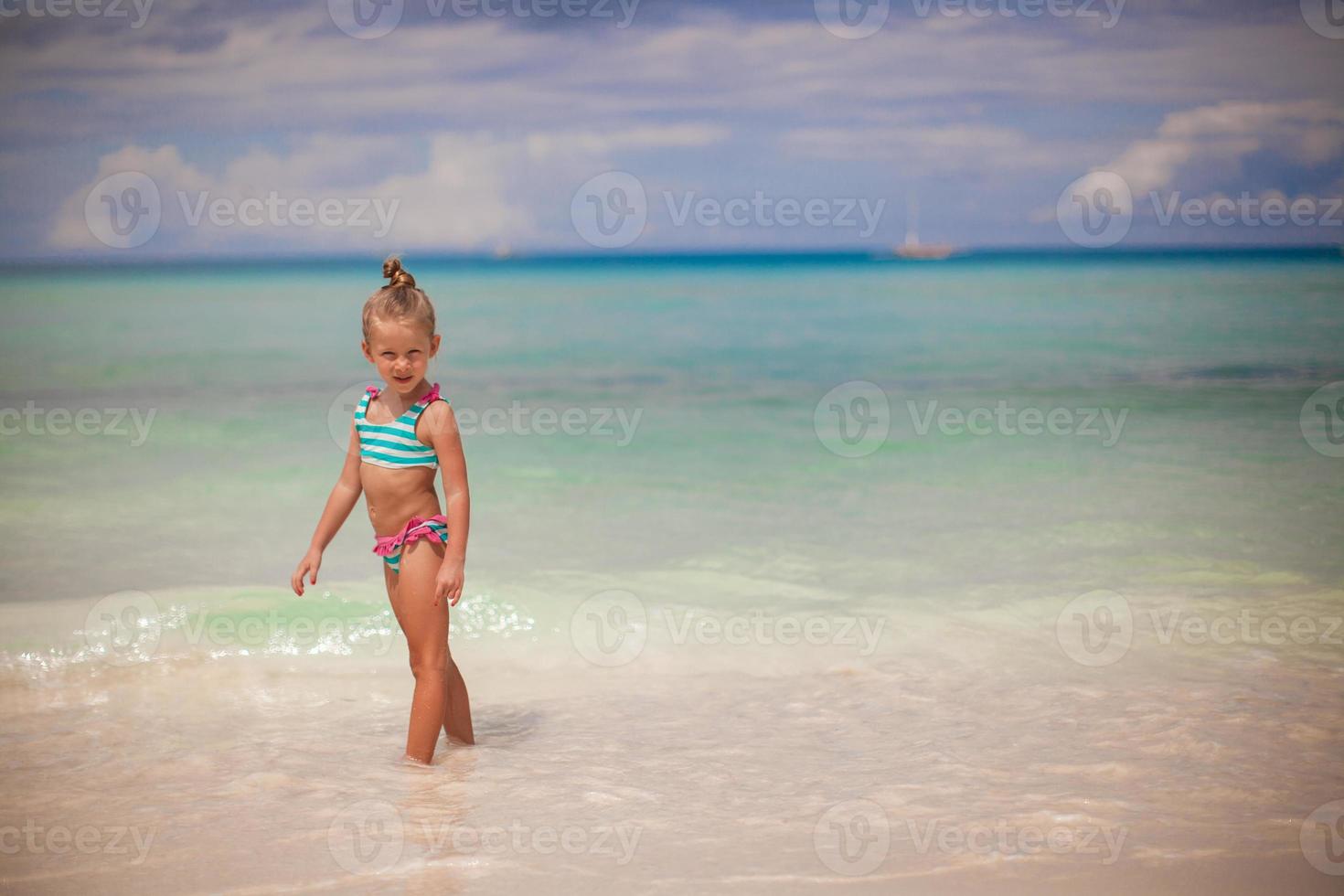 Adorable little girl walking in the water on tropical beach vacation photo