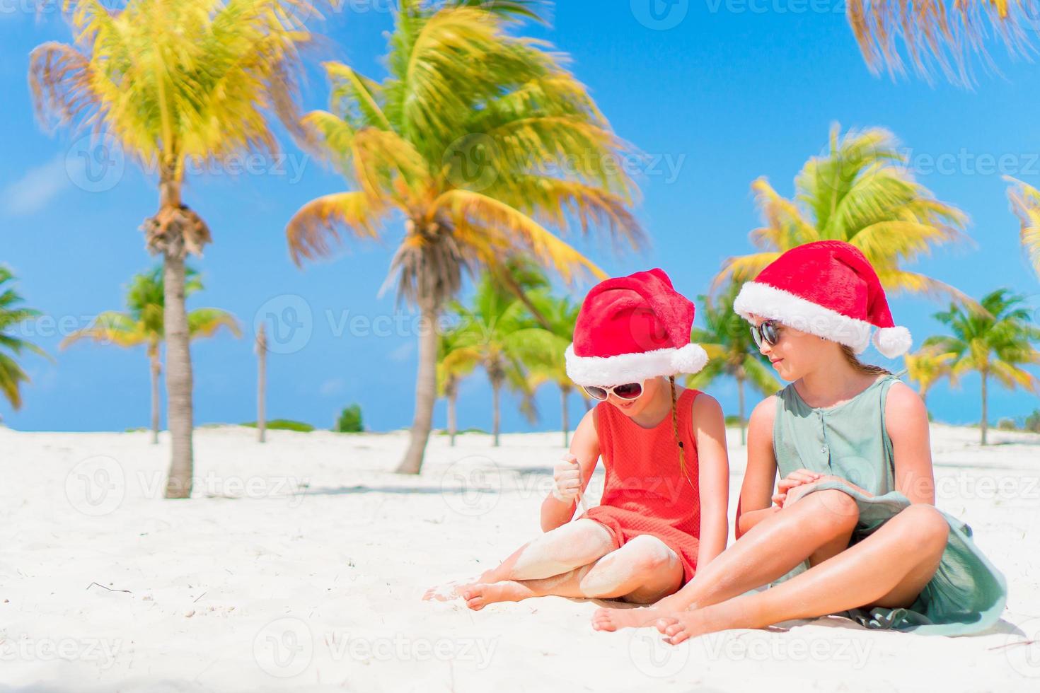 Adorable little kids have fun in Santa hat during Christmas beach vacation. New Year on the beach photo