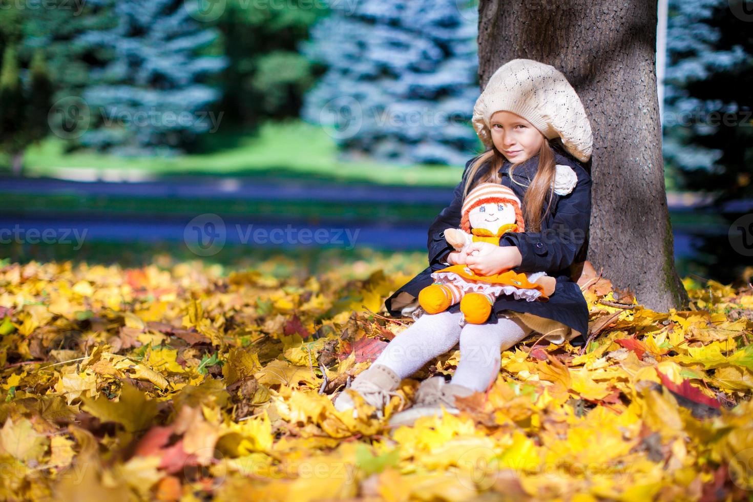 Pretty Fashion girl sits under a maple tree with doll on sunny autumn day photo