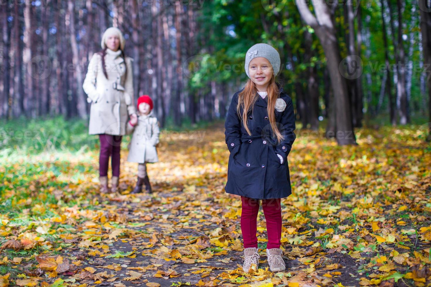 en primer plano hay una hermosa y dulce niña detrás de su madre y su hermana en el parque de otoño foto