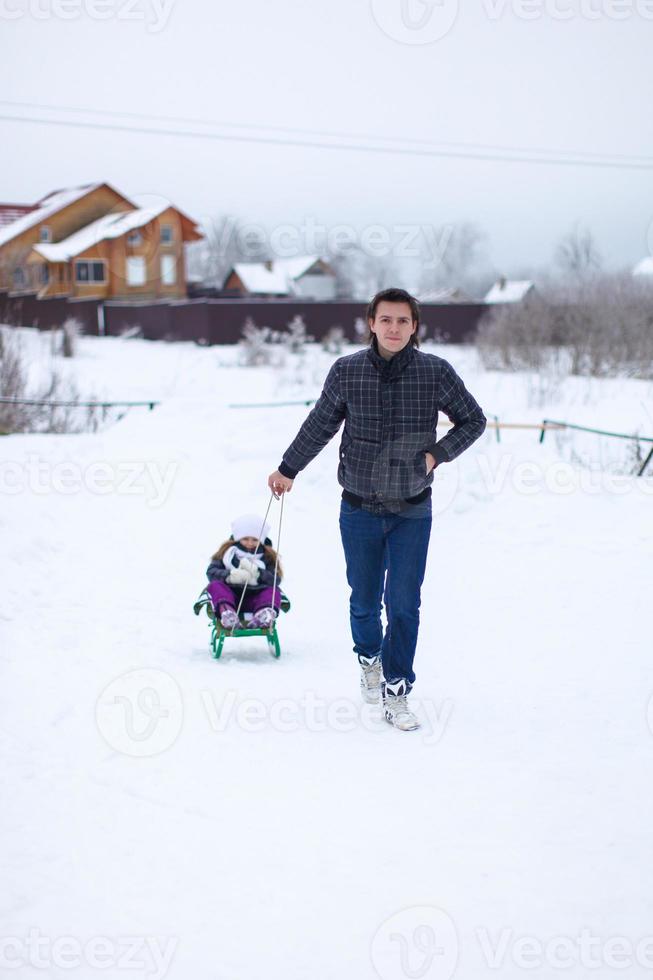 Young dad rolls his little cute daughter on a sled in the snow outdoors photo