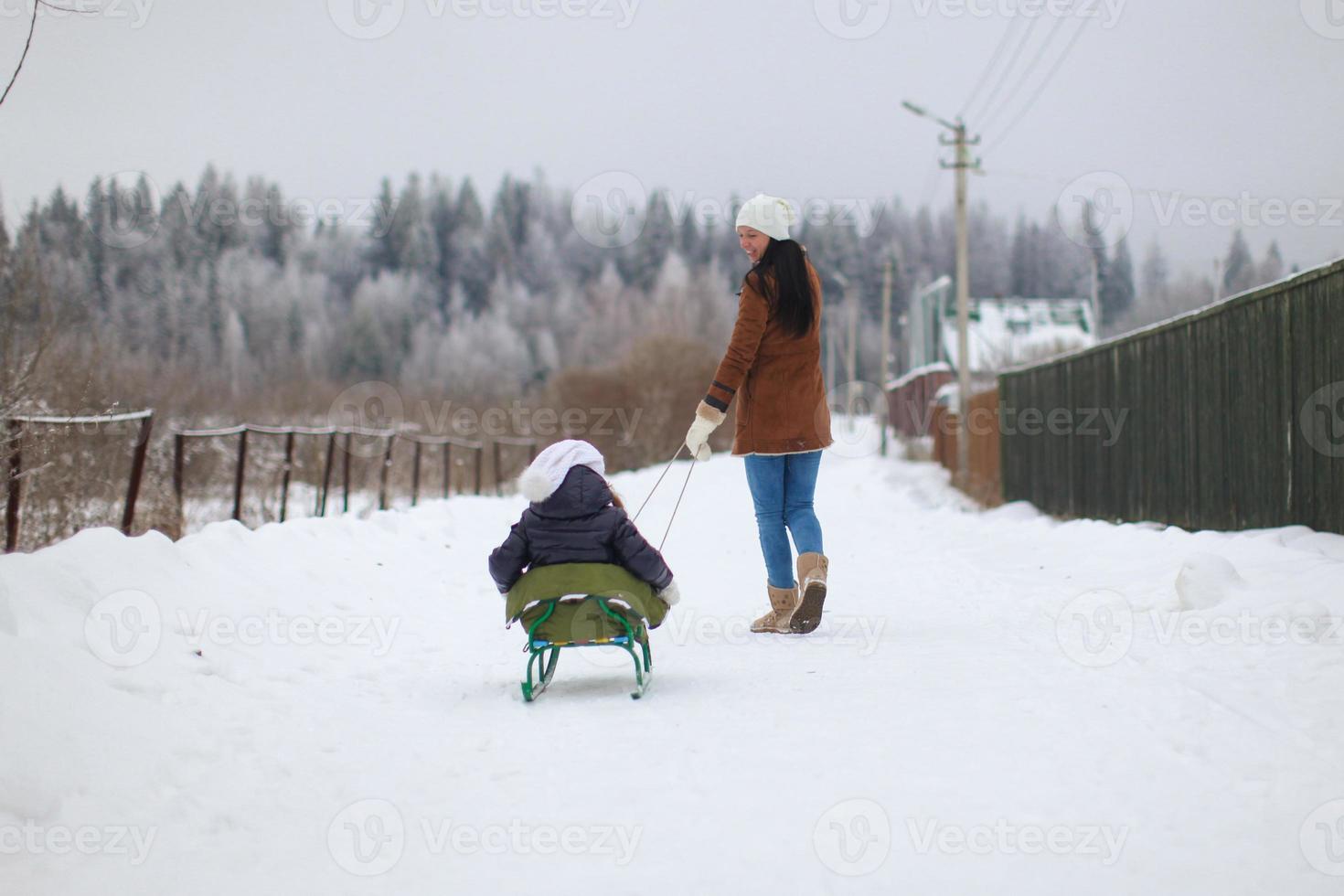 Young mother rolls her little cute daughters on a sled in winter day photo