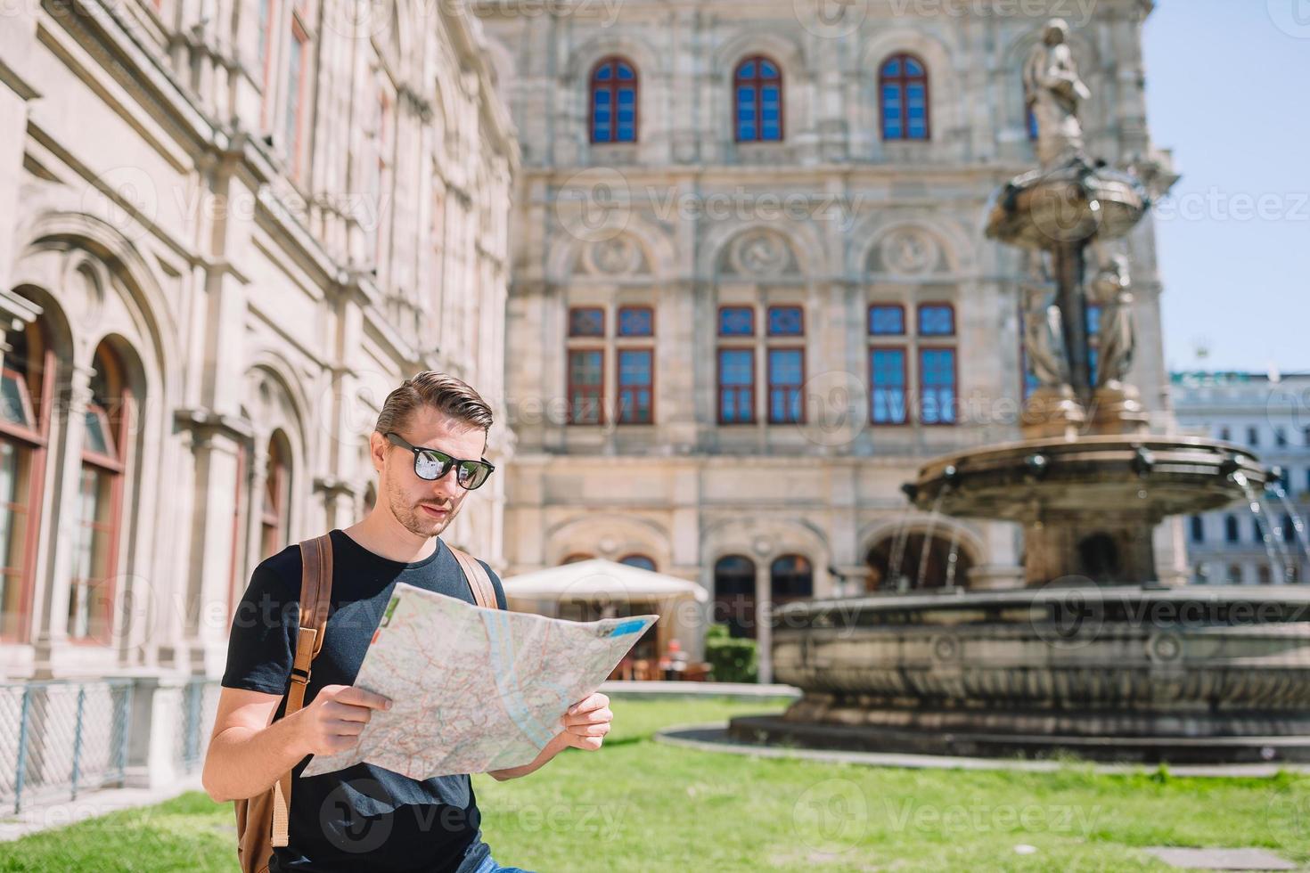 Man tourist with a city map and backpack in Europe street. Caucasian boy looking with map of European city. photo