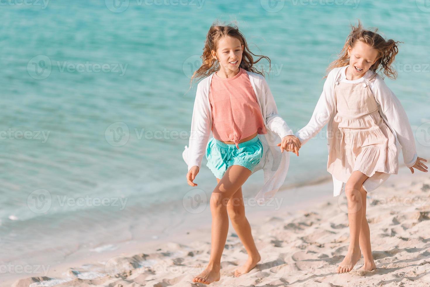 Little happy funny girls have a lot of fun at tropical beach playing together. photo