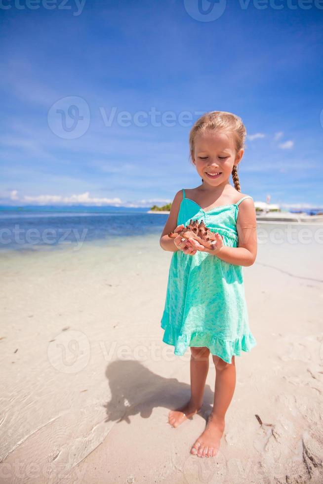 Little adorable girl with starfish in her hands at the tropical beach photo