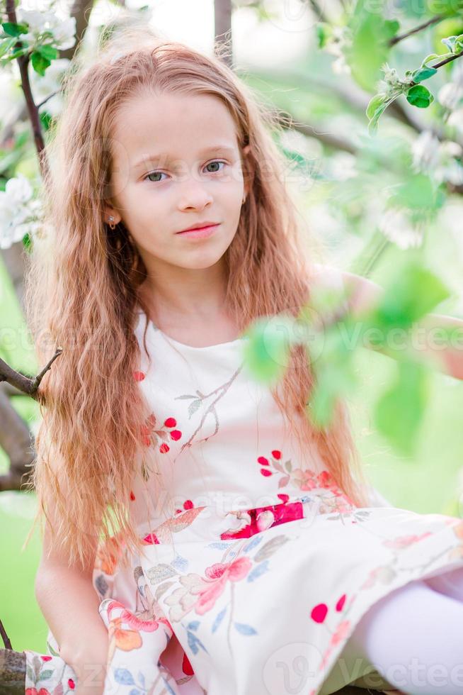 Adorable little girl in blooming apple tree garden on spring day photo