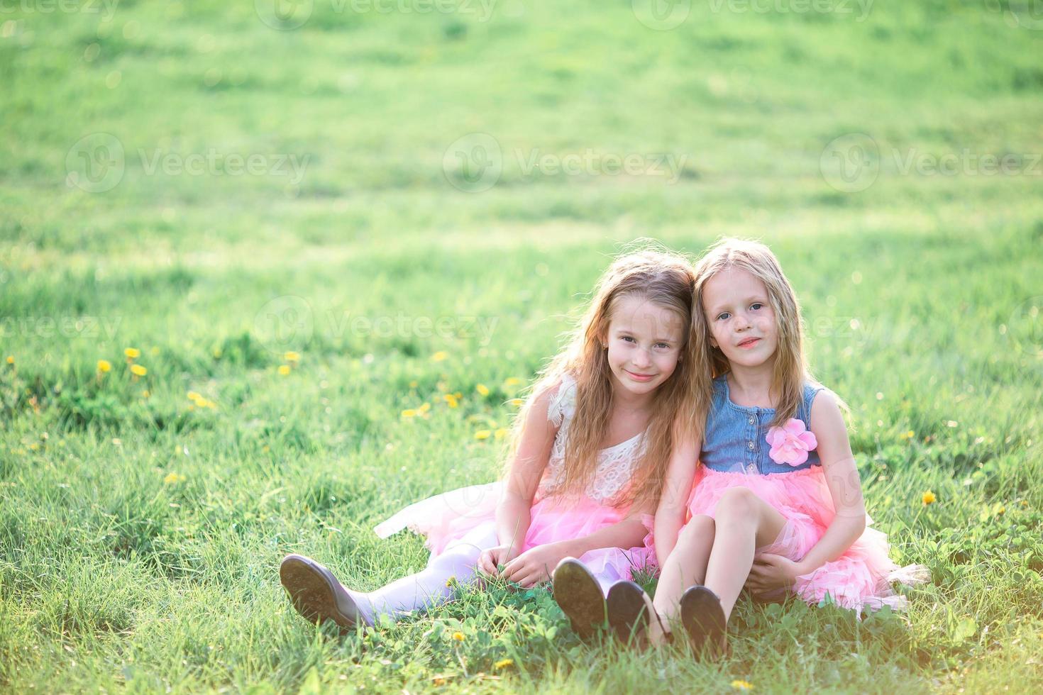 Adorable little girls on spring day outdoors sitting on the grass photo