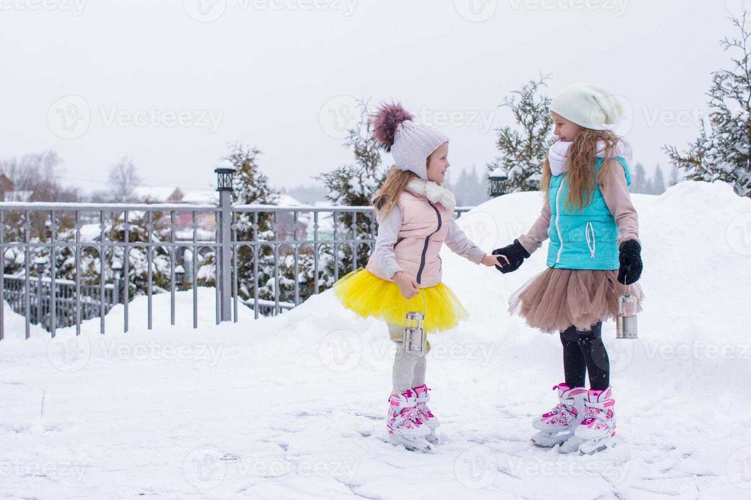 Little girls skating on ice rink outdoors in winter snow day photo