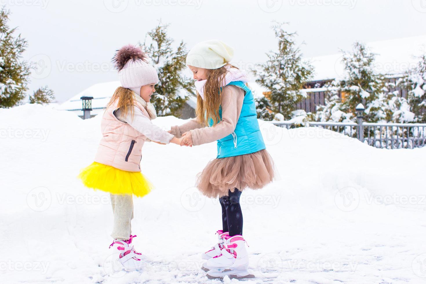 Little girls skating on ice rink outdoors in winter snow day photo