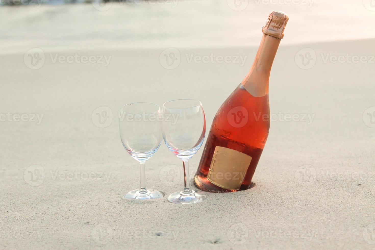botella de vino tinto y dos copas en la playa de arena blanca foto