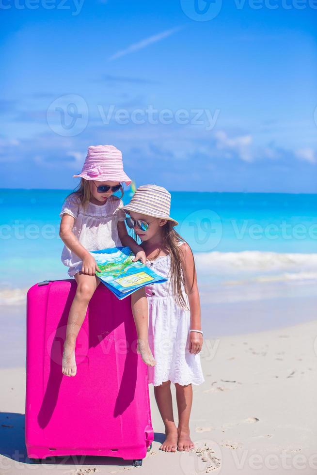 Little girls with big suitcase and map on tropical beach photo